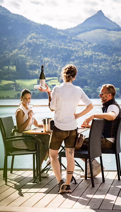 Bedienung auf Seeterrasse mit Gästen und Weinflasche