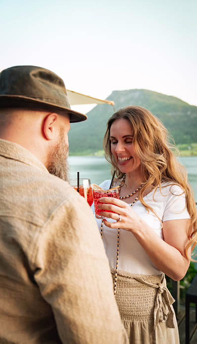 Ein paar mit einem Cocktail in der Hand, dahinter See und Berge